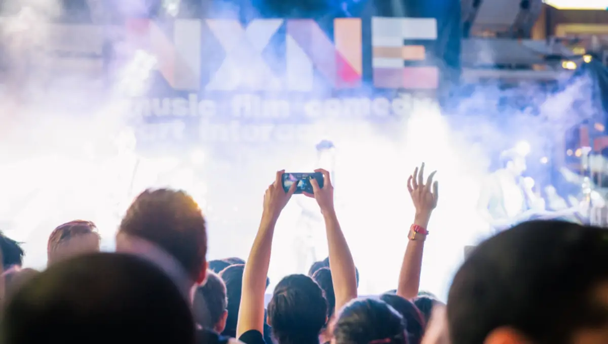 Festival crowd filming a lit stage on a phone